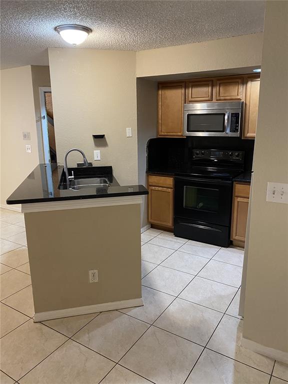 A kitchen features light wood cabinets, black countertops, and black appliances over tiled floors — 4524 COMMANDER DRIVE UNIT 1615, ORLANDO, FL