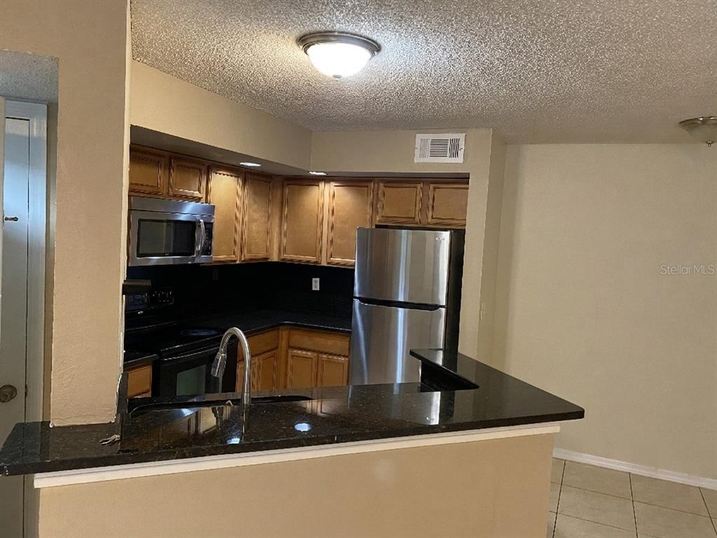 A kitchen features wood cabinets, stainless steel appliances, and a dark granite breakfast bar — 4524 COMMANDER DRIVE UNIT 1615, ORLANDO, FL