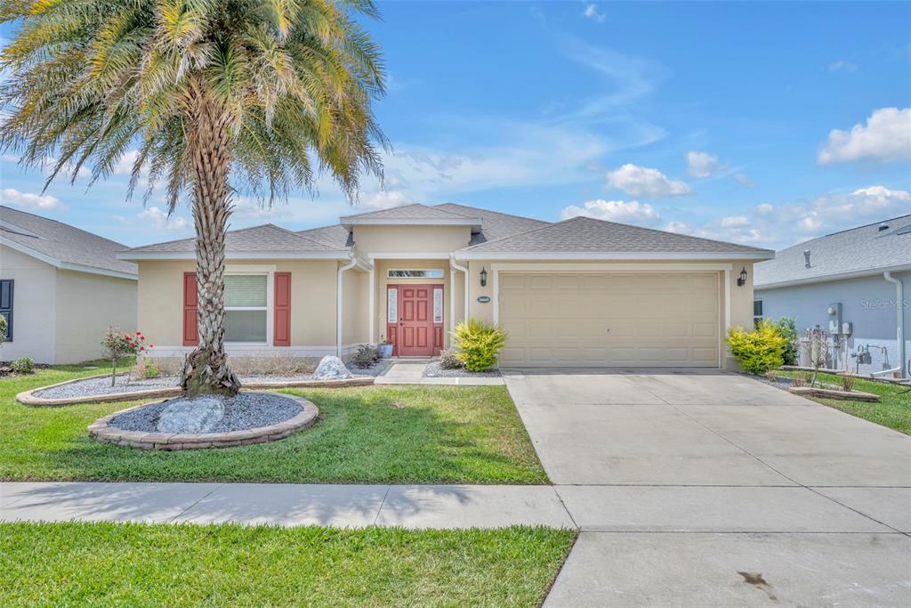 A single-story suburban house with a tan exterior, red front door, and a palm tree — 26669 OTTER CREEK LANE, LEESBURG, FL