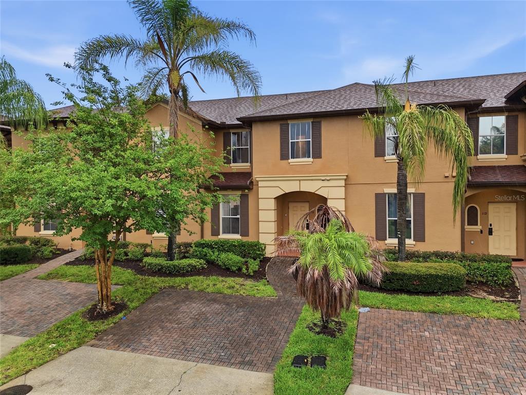 A two-story tan townhouse with brown shutters, a brick driveway, and palm trees in front — 122 CAPRI DRIVE, DAVENPORT, FL