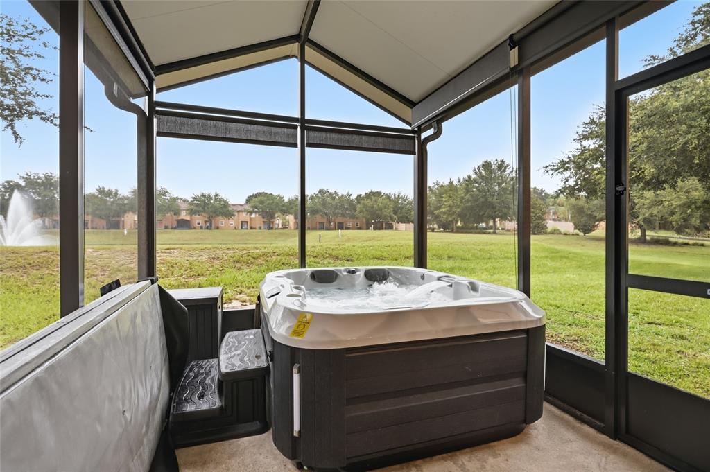 A hot tub sits on a screened-in patio overlooking a grassy lawn and a fountain — 122 CAPRI DRIVE, DAVENPORT, FL