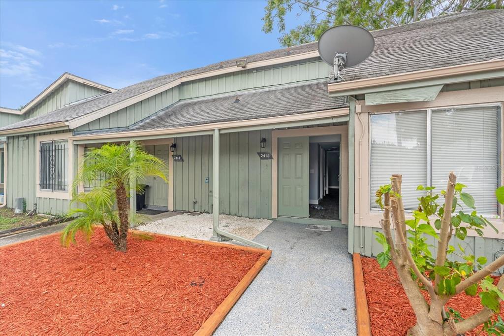 The exterior of a single-story home features green vertical siding, a walkway, and landscaping — 2418 SKAN COURT UNIT C, ORLANDO, FL