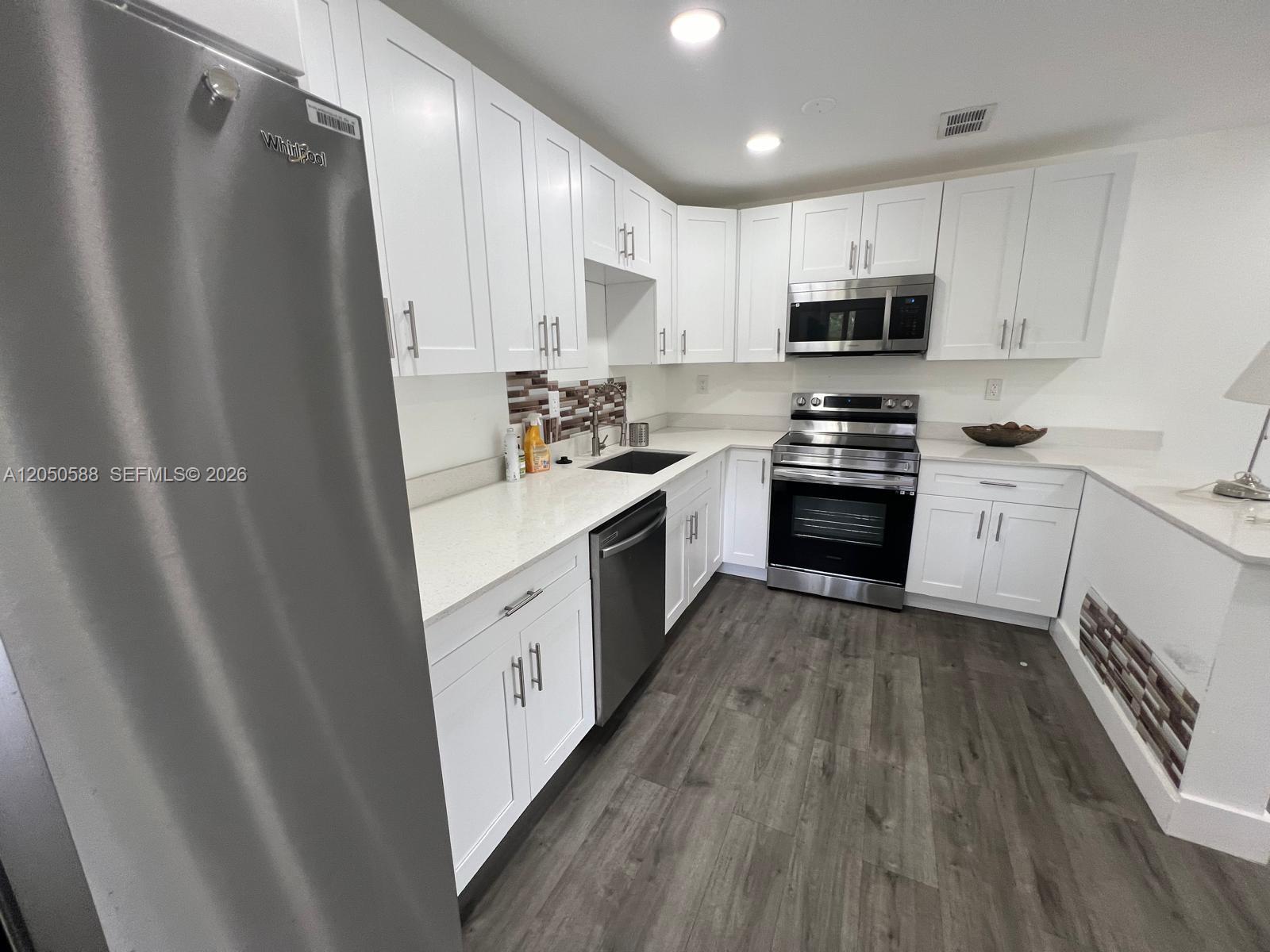 A kitchen features white cabinets, stainless steel appliances, quartz countertops, and wood-look flooring — 4111 Stirling Rd # 209, Dania Beach FL 33314, DANIA BEACH, FL