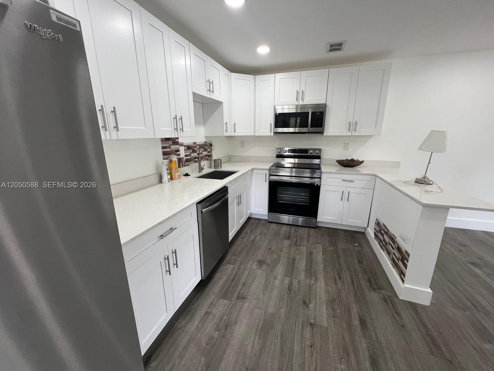 A modern kitchen features white cabinets, stainless steel appliances, and gray wood-look flooring — 4111 Stirling Rd # 209, Dania Beach FL 33314, DANIA BEACH, FL