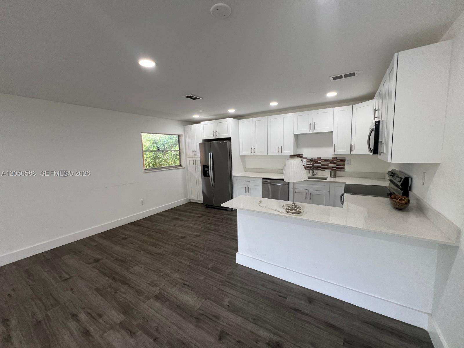 A kitchen features white cabinets, stainless steel appliances, quartz countertops, and dark wood-look flooring — 4111 Stirling Rd # 209, Dania Beach FL 33314, DANIA BEACH, FL