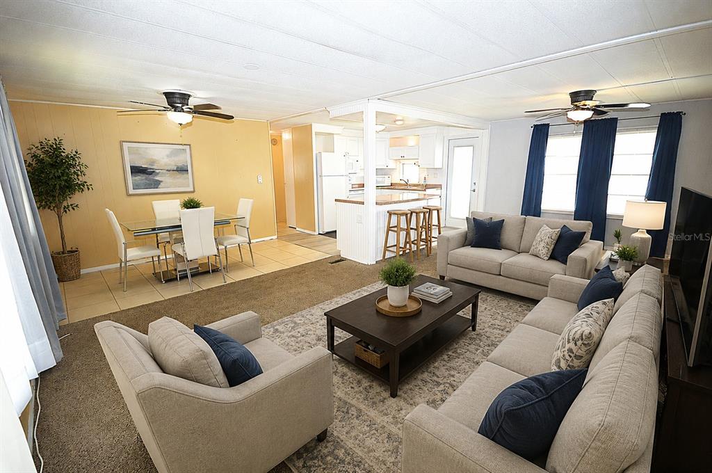 An open-concept living and dining area features neutral furniture, carpeted floors, and a kitchen island — 115 RACHEL DRIVE, TARPON SPRINGS, FL