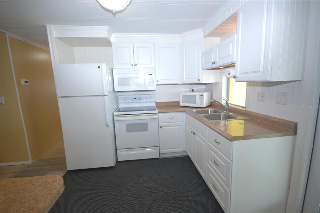A kitchen features white cabinets, white appliances, a tan countertop, and dark gray flooring — 115 RACHEL DRIVE, TARPON SPRINGS, FL