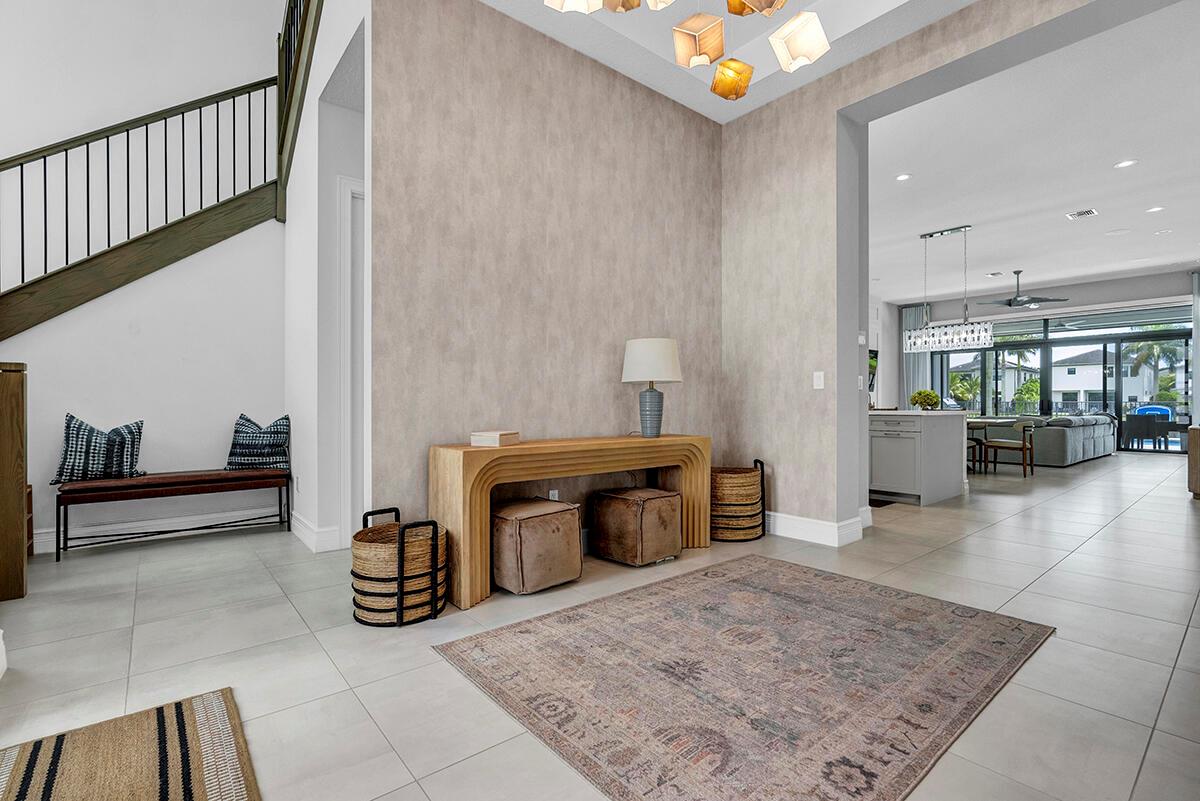 A modern entryway features a wooden console table, textured wallpaper, and a staircase with railings — 9046 Chauvet Way, Boca Raton FL 33496, BOCA RATON, FL