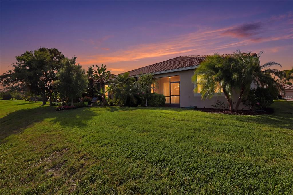 A single-story house with a screened lanai sits on a grassy lawn at sunset — 11929 TAPESTRY LN, VENICE, FL