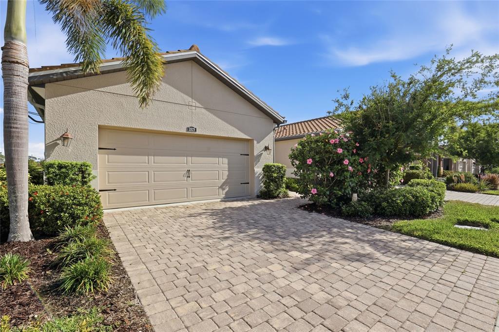 A beige house exterior features a two-car garage, a paved driveway, and landscaping — 11929 TAPESTRY LN, VENICE, FL