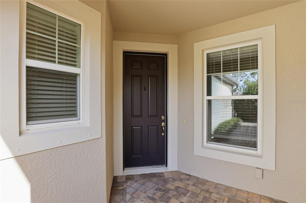 A dark brown front door is centered between two windows on a paved entryway — 11929 TAPESTRY LN, VENICE, FL