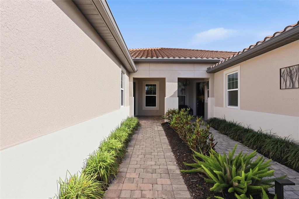 A paved walkway leads to the recessed front entryway of a beige stucco house — 11929 TAPESTRY LN, VENICE, FL