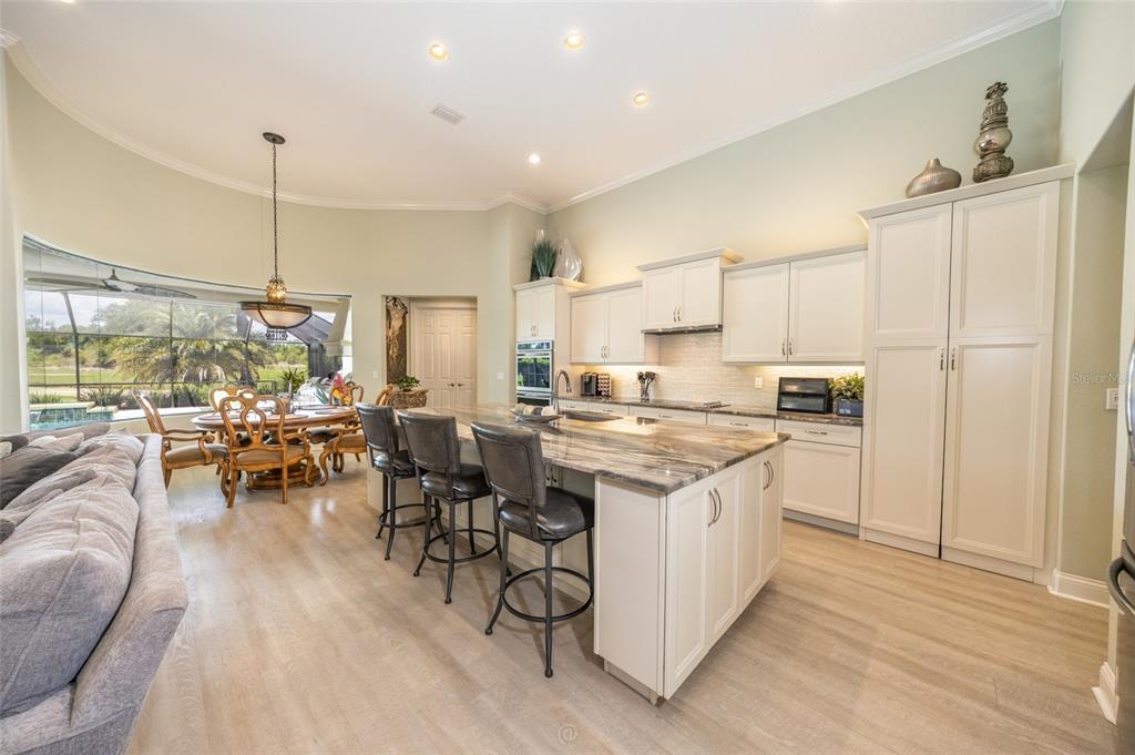 A kitchen with white cabinets, a stone-topped island, and bar seating overlooks a dining area — 478 SWEETGUM LANE, PALM COAST, FL