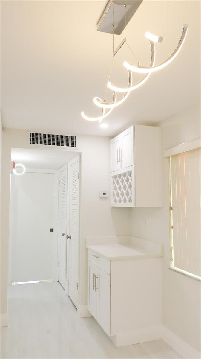A white wet bar area features a wine rack, cabinetry, and a modern spiral chandelier — 343 Normandy H # 343, Delray Beach FL 33484, DELRAY BEACH, FL