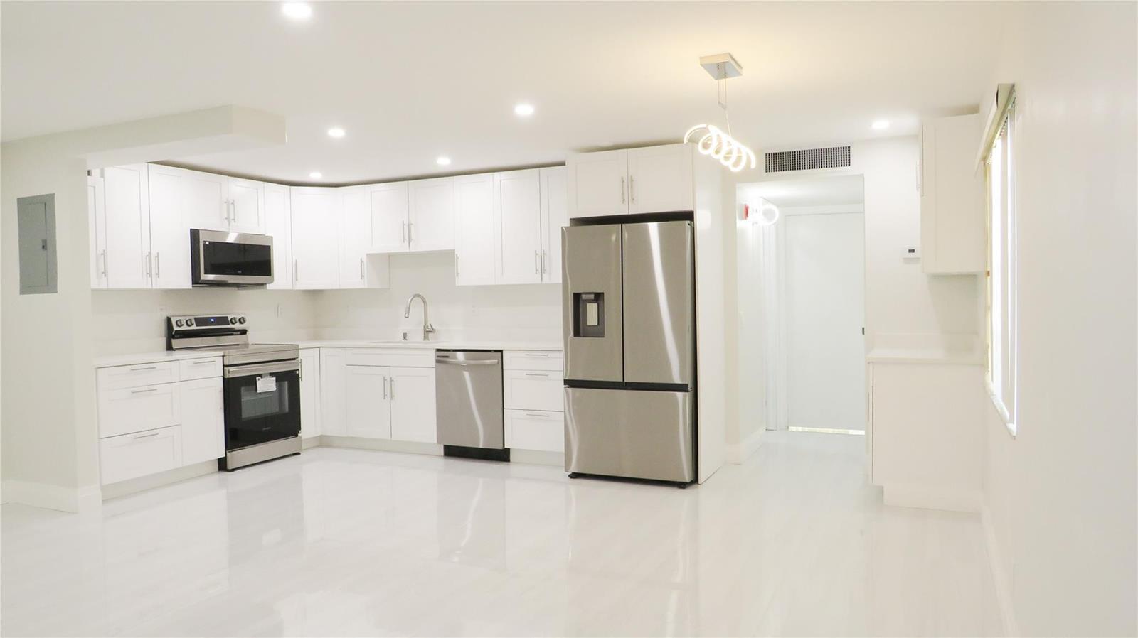 A modern kitchen features white cabinetry, stainless steel appliances, and glossy white tile flooring — 343 Normandy H # 343, Delray Beach FL 33484, DELRAY BEACH, FL