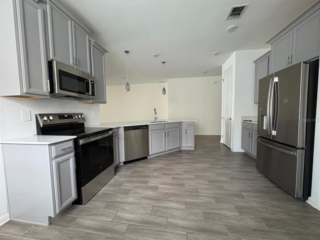 A kitchen features gray cabinets, stainless steel appliances, white countertops, and wood-look tile flooring — 2710 SLASH WAY, ST CLOUD, FL