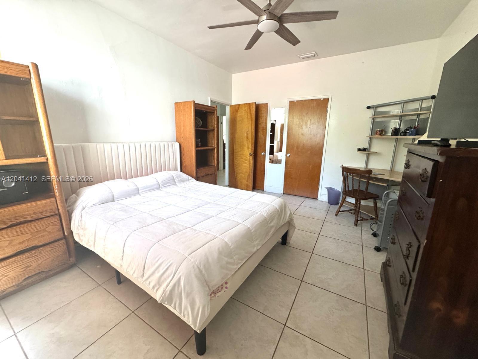 A bedroom features a bed, wooden furniture, a desk, and a ceiling fan on tile floors — BAY HARBOR ISLANDS, FL