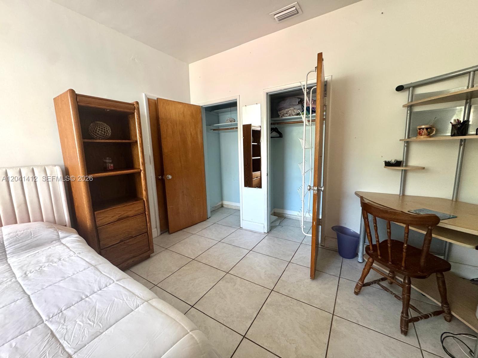 A bedroom features a bed, a wooden bookshelf, two closets, and a desk with a chair — BAY HARBOR ISLANDS, FL