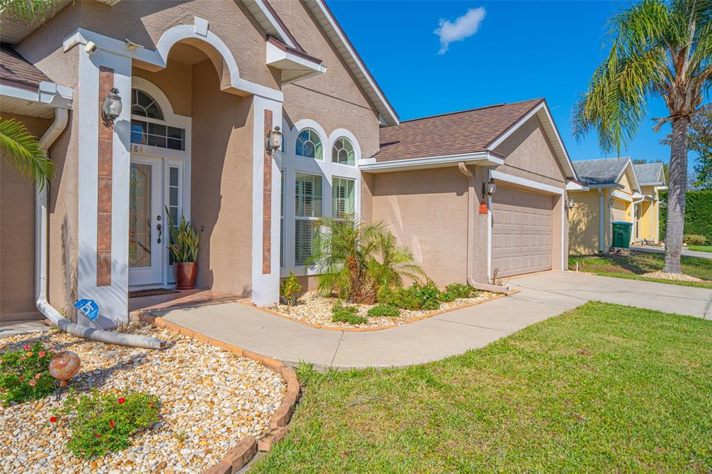 A tan stucco house features a front entrance, a garage, and a landscaped front yard — 484 KETTERING ROAD, DELTONA, FL