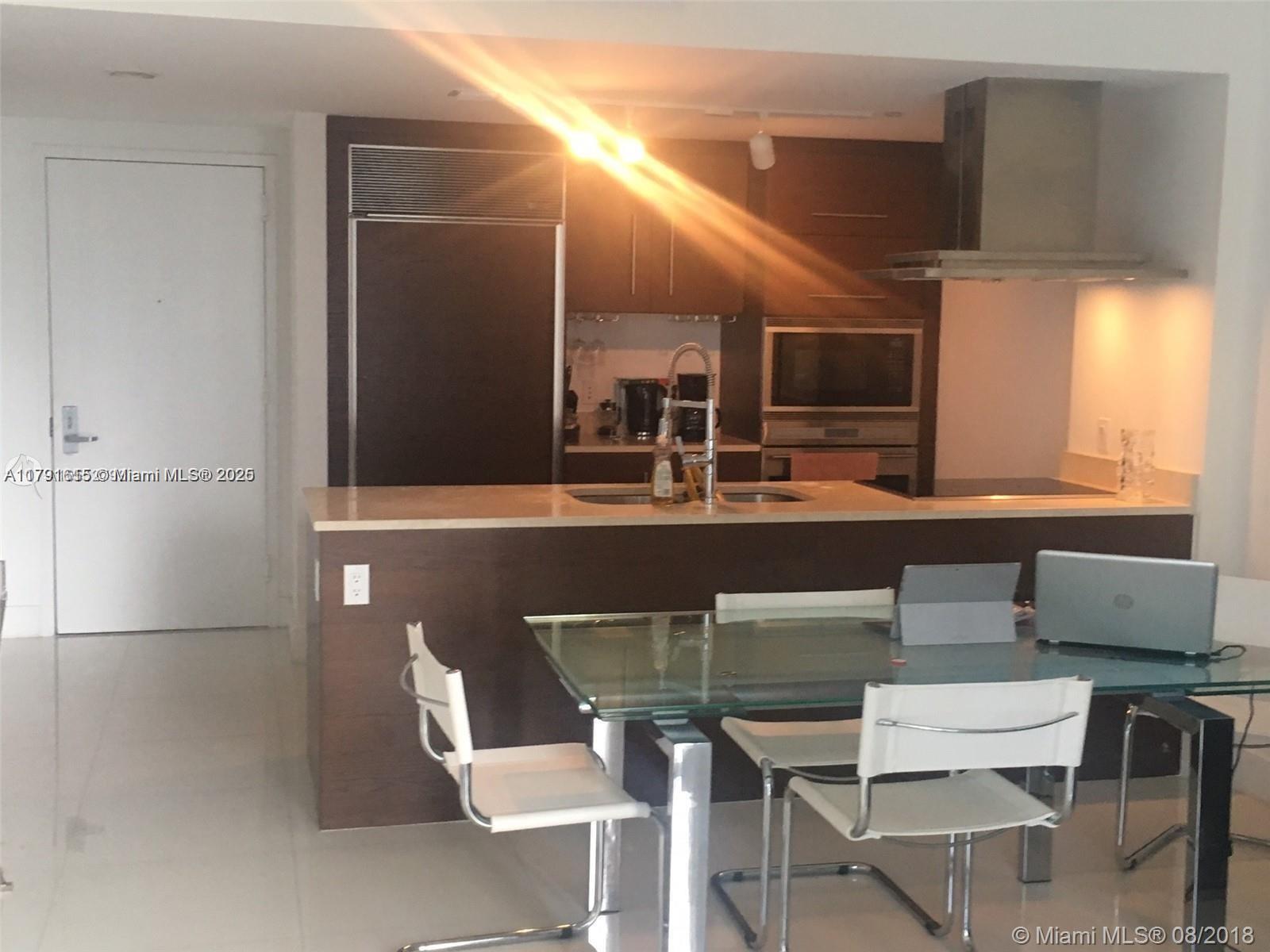 A kitchen with dark wood cabinetry, stainless steel appliances, and a glass-topped dining table — 485 Brickell Ave # 1903, Miami FL 33131, MIAMI, FL