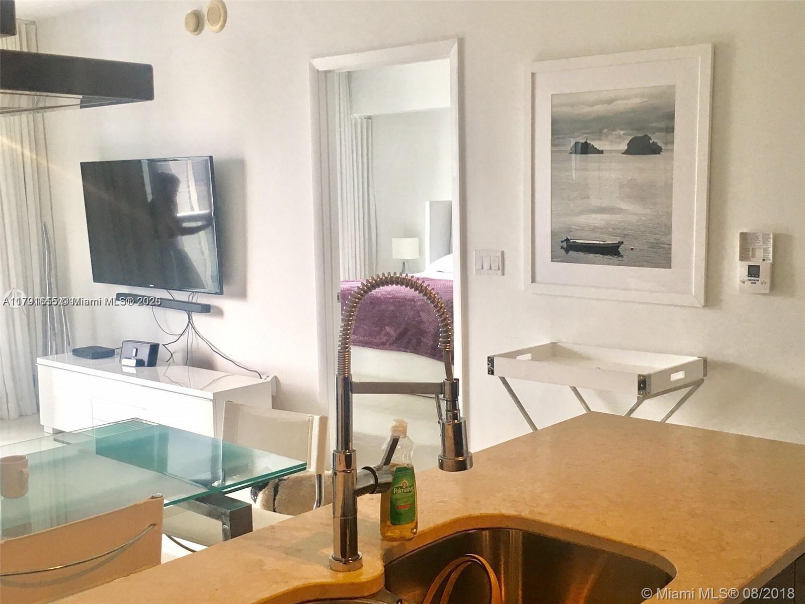 A kitchen island with a stainless steel sink overlooks a living area and bedroom doorway — 485 Brickell Ave # 1903, Miami FL 33131, MIAMI, FL