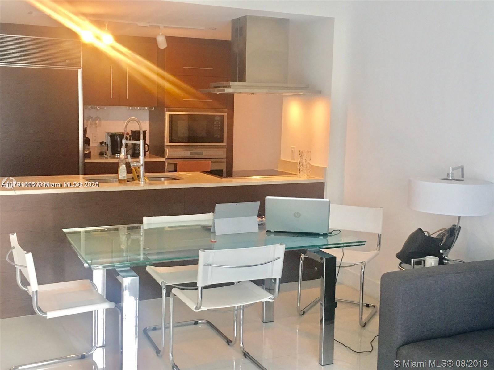 A modern kitchen with dark wood cabinetry and a glass dining table sits in an apartment — 485 Brickell Ave # 1903, Miami FL 33131, MIAMI, FL