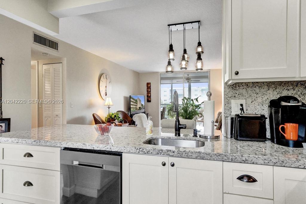 A kitchen island with a granite countertop and stainless steel sink overlooks a living area — 415 SE 11th Ter # 207, Dania Beach FL 33004, DANIA BEACH, FL