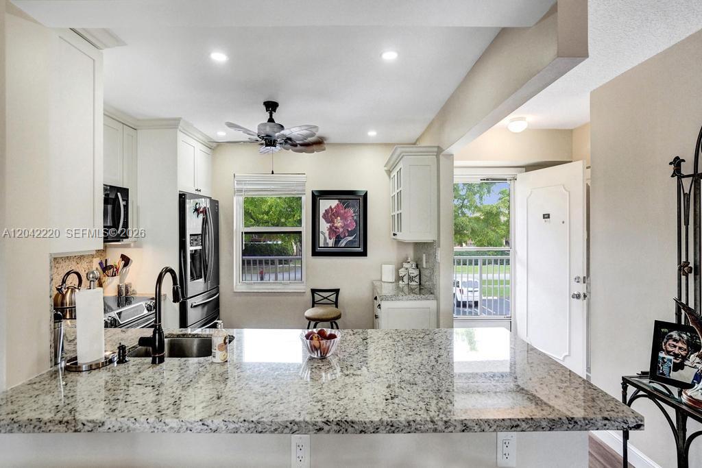 A kitchen features white cabinets, granite countertops, a breakfast bar, and a view of greenery — 415 SE 11th Ter # 207, Dania Beach FL 33004, DANIA BEACH, FL