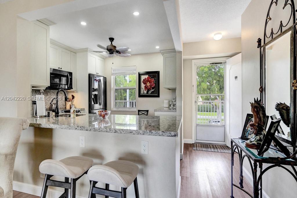 A kitchen with granite countertops and bar seating overlooks an entryway with a glass door — 415 SE 11th Ter # 207, Dania Beach FL 33004, DANIA BEACH, FL