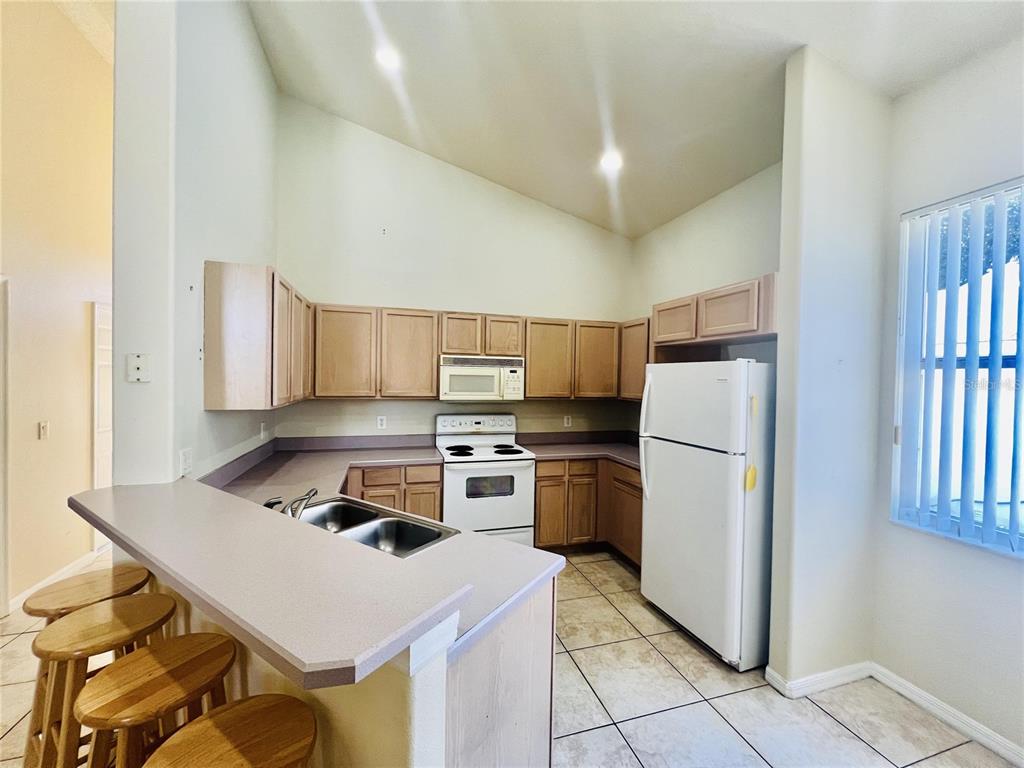 A kitchen features light wood cabinets, white appliances, a breakfast bar, and tile flooring — 2565 BEAR CREEK COURT, KISSIMMEE, FL
