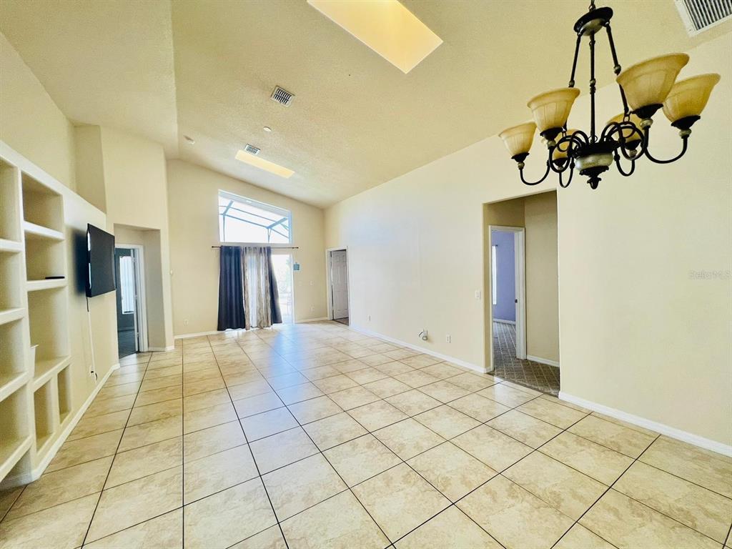 A spacious living room features tile flooring, a vaulted ceiling, a chandelier, and built-in shelving — 2565 BEAR CREEK COURT, KISSIMMEE, FL