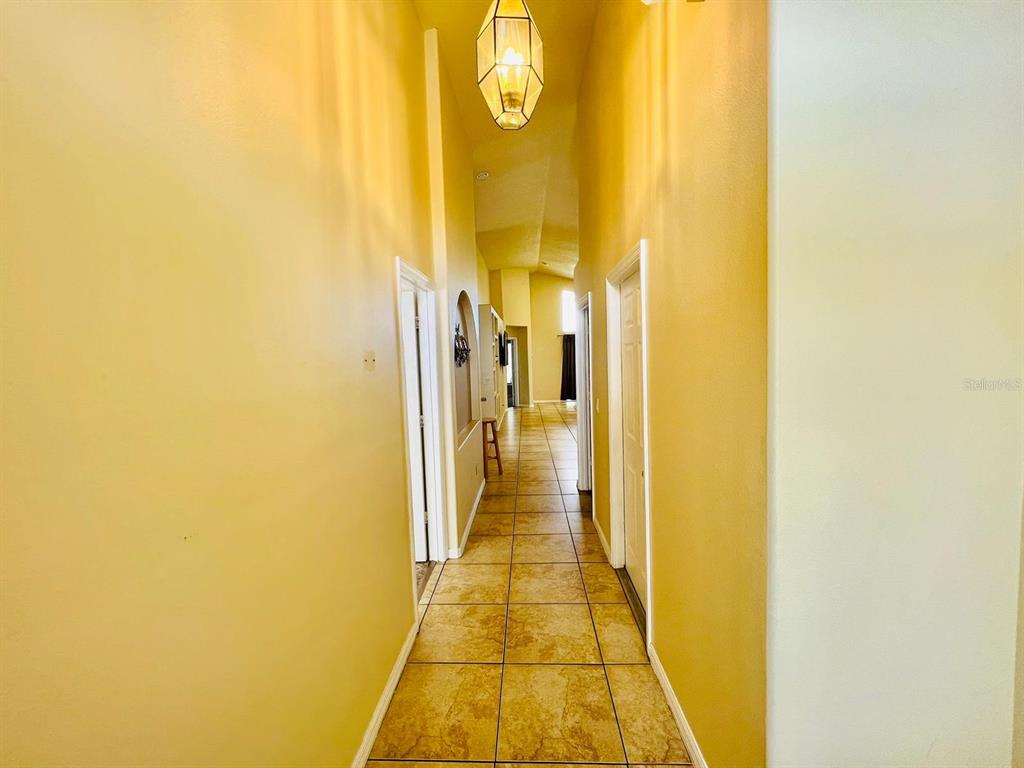 A long hallway with yellow walls, tile flooring, and a hanging lantern light fixture — 2565 BEAR CREEK COURT, KISSIMMEE, FL