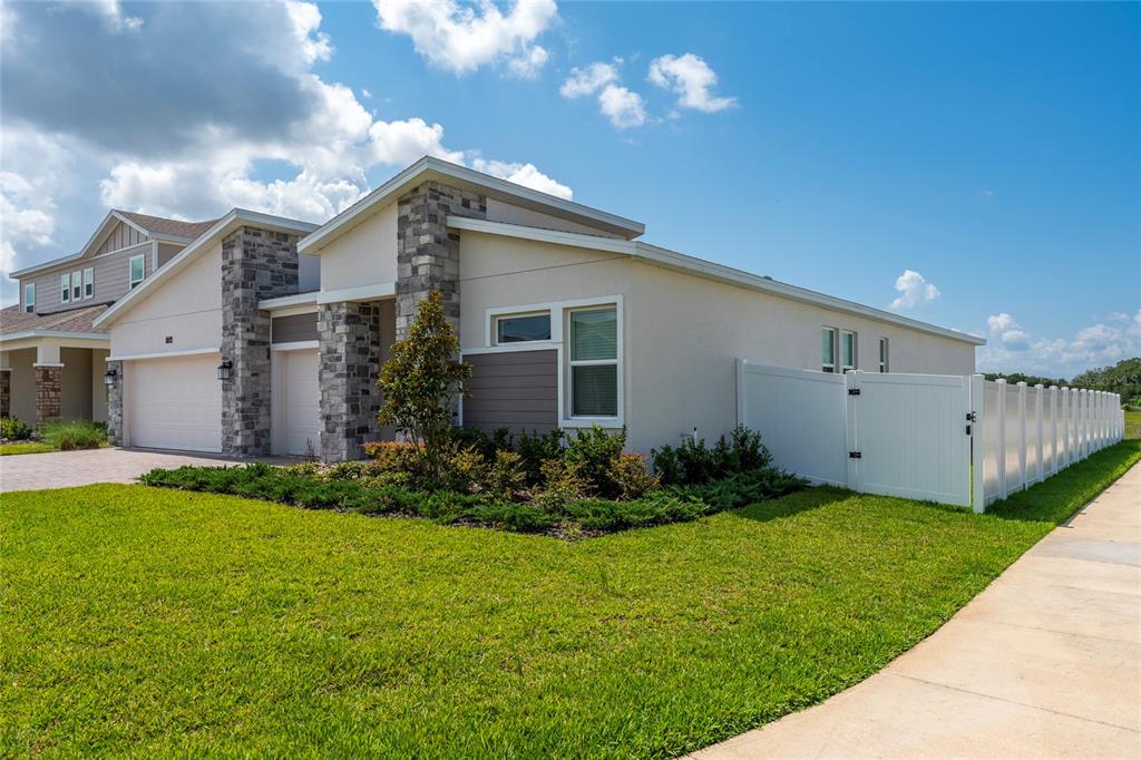 A modern single-story house with a stone-accented facade, a two-car garage, and a white fence — 1744 RIDER RAIN LANE, APOPKA, FL