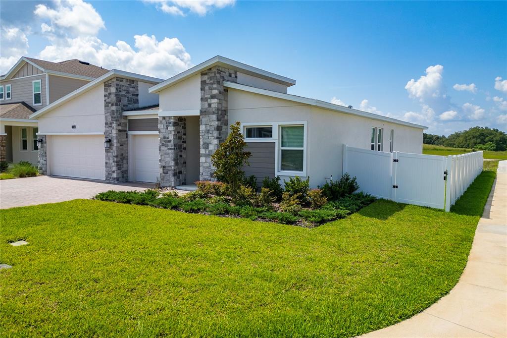 A modern single-story house with a stone-accented facade, a two-car garage, and a white fence — 1744 RIDER RAIN LANE, APOPKA, FL