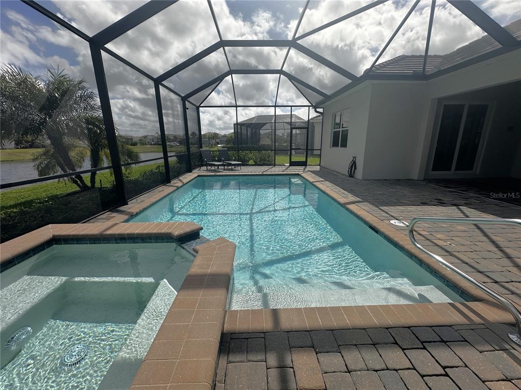A screened-in swimming pool and spa with paver decking overlooking a pond — 14897 CHERRY BLOSSOM WAY, PUNTA GORDA, FL