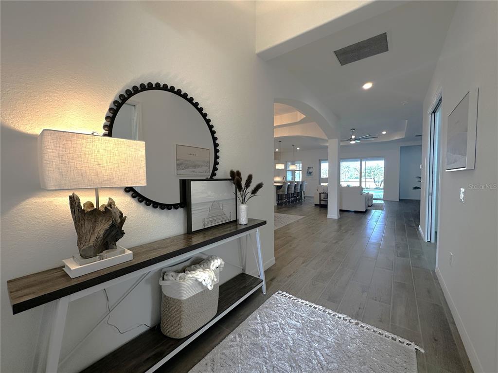 A bright entryway features a console table, a round mirror, and a view into the living area — 14897 CHERRY BLOSSOM WAY, PUNTA GORDA, FL