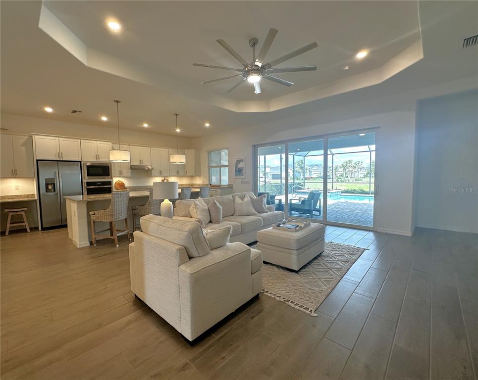 An open-concept living room and kitchen feature light wood floors, white cabinetry, and a pool view — 14897 CHERRY BLOSSOM WAY, PUNTA GORDA, FL