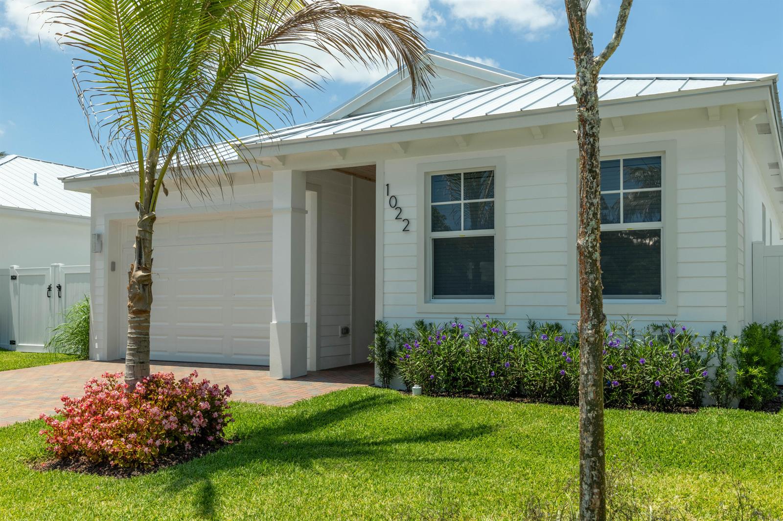 A white single-story house with a metal roof, garage, and landscaped front yard — 1022 Miami Boulevard, Delray Beach FL 33483, DELRAY BEACH, FL
