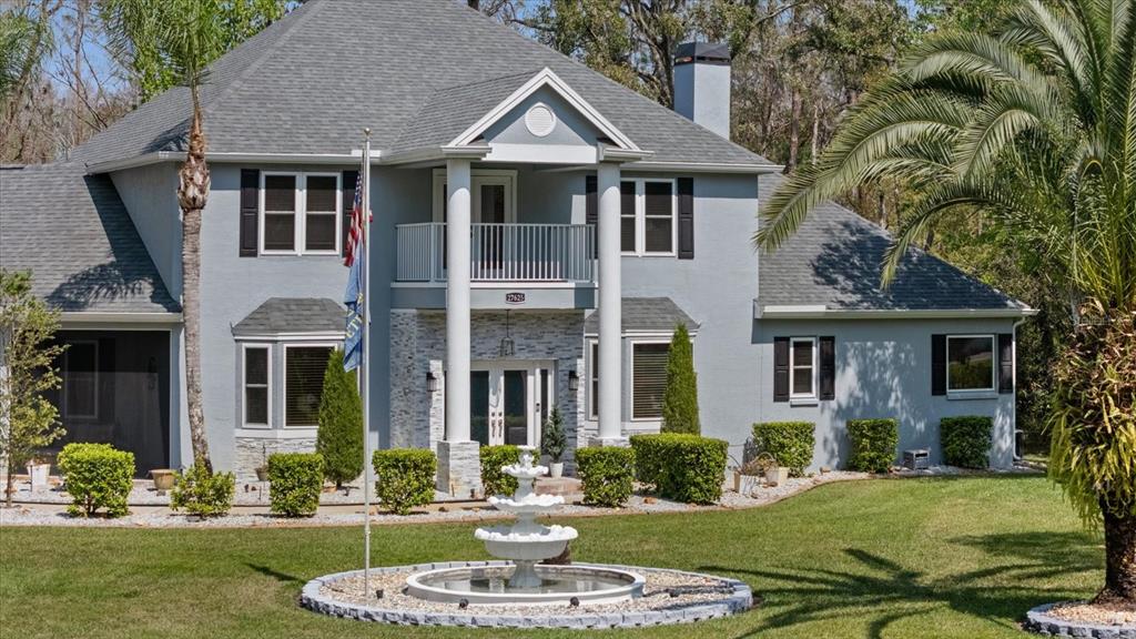 A two-story gray house with a white-columned entrance, balcony, and manicured landscaping — 27625 LINCOLN PLACE, WESLEY CHAPEL, FL