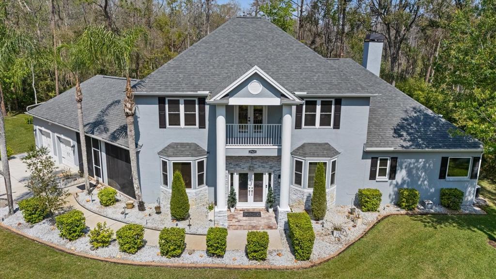 A two-story gray house with a front balcony, white columns, and stone accents — 27625 LINCOLN PLACE, WESLEY CHAPEL, FL
