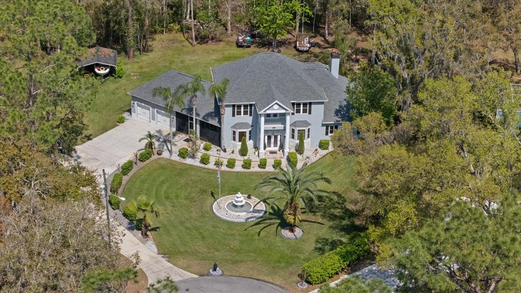 A two-story gray house with a columned entryway, balcony, and stone accents sits on a lawn — 27625 LINCOLN PLACE, WESLEY CHAPEL, FL