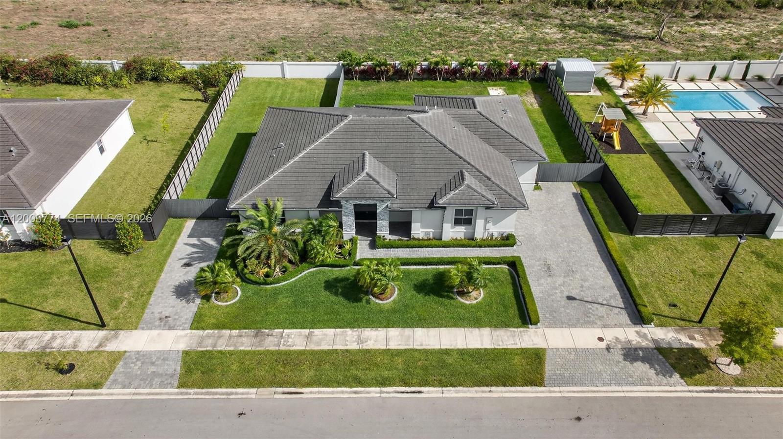 An aerial view shows a single-story house with a gray tile roof and paved driveway — HOMESTEAD, FL