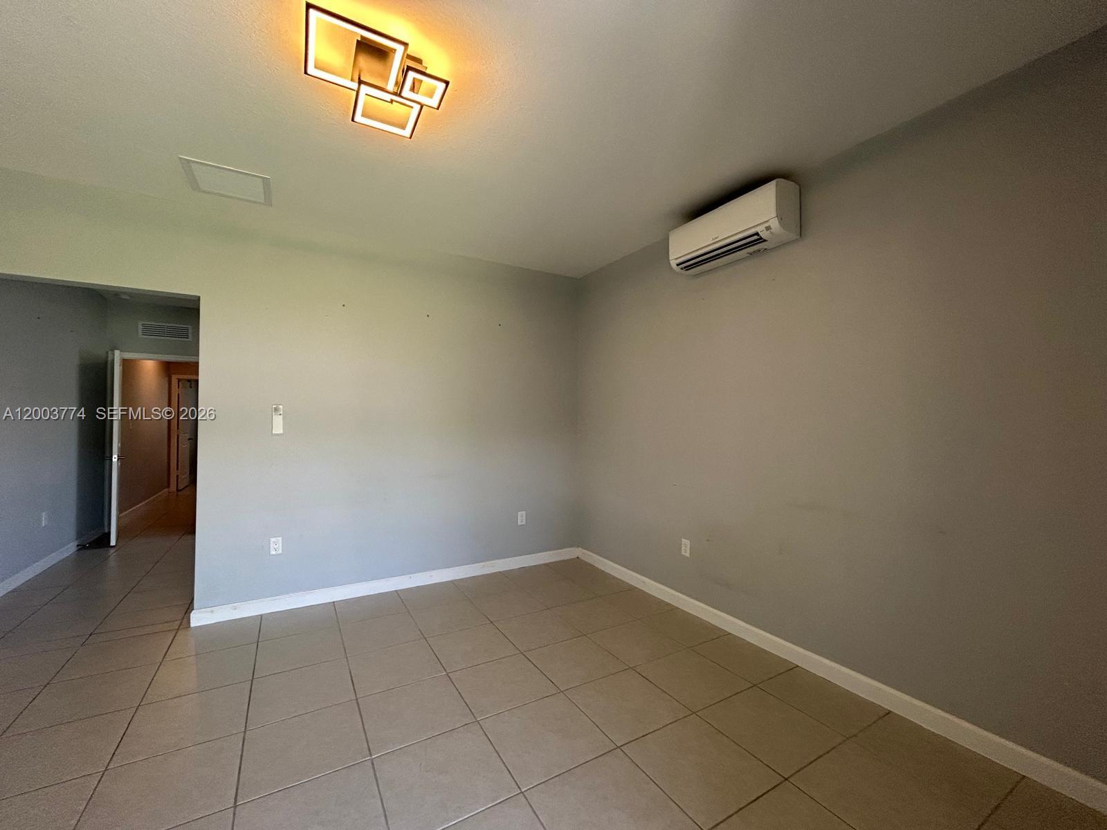 An empty room with tile flooring, a wall-mounted air conditioner, and a modern ceiling light — HOMESTEAD, FL