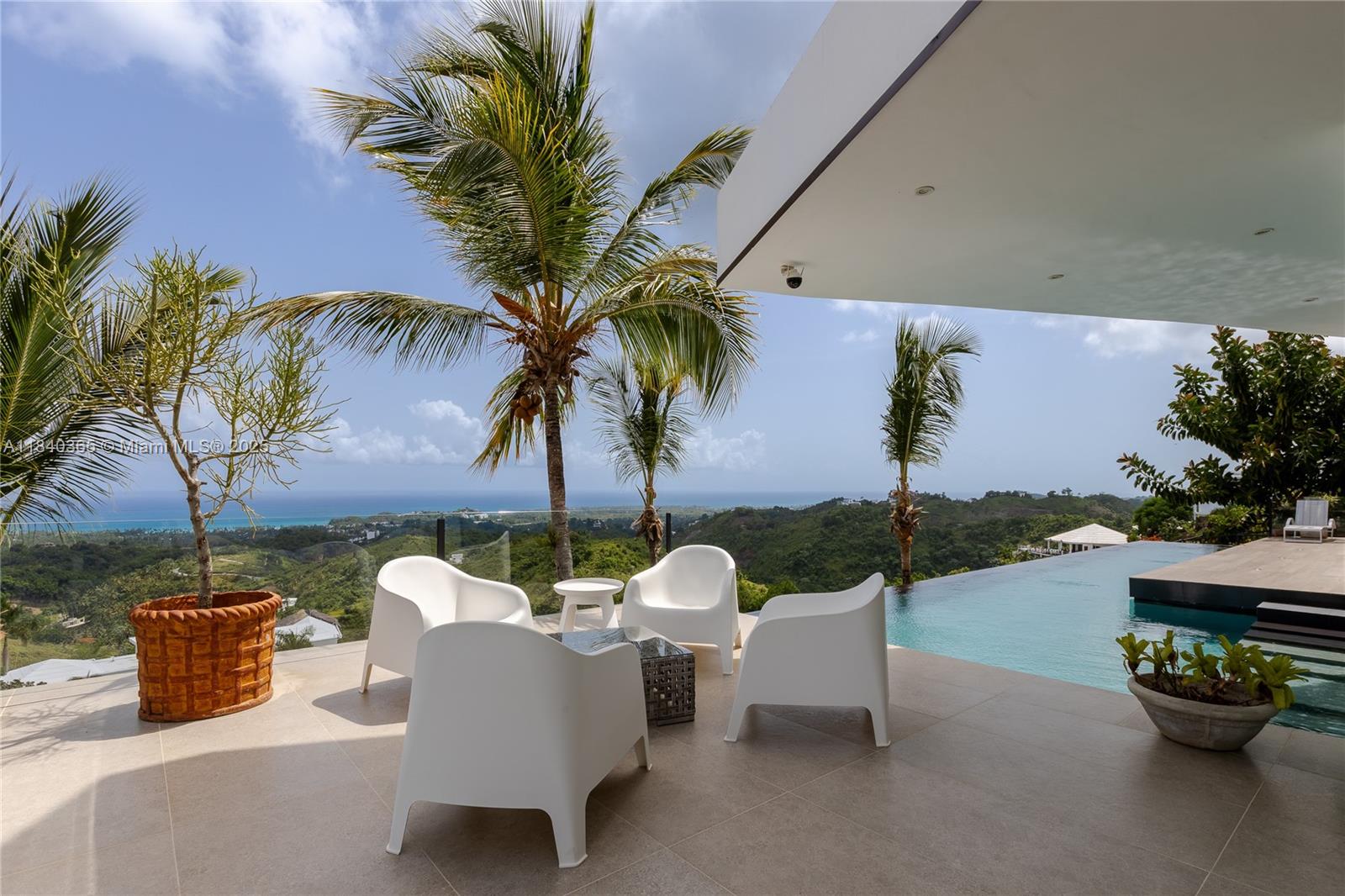 A modern patio features white chairs, a small table, and an infinity pool overlooking hills — Palmar de los Nidos LAS TERRENAS, SAMANA, FL 32000, FL