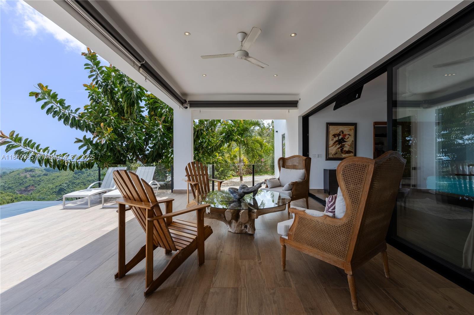 A covered outdoor patio features wooden furniture, a glass-topped table, and a view of hills — Palmar de los Nidos LAS TERRENAS, SAMANA, FL 32000, FL