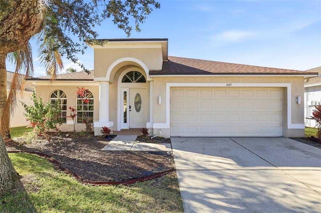 A single-story house with a beige stucco exterior, arched windows, and a two-car garage — 4145 MEDBURY DRIVE, WESLEY CHAPEL, FL