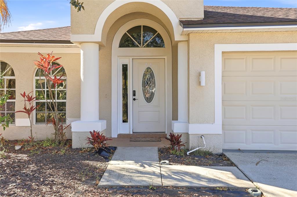 The exterior of a house features a beige stucco facade, a white arched entryway, and a garage — 4145 MEDBURY DRIVE, WESLEY CHAPEL, FL