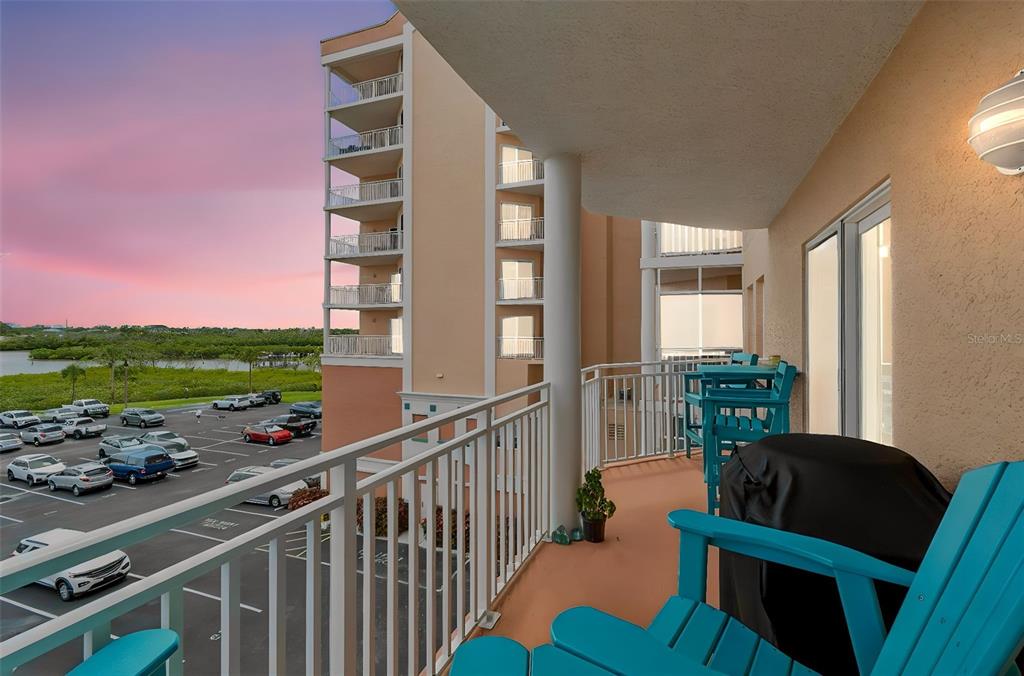 A balcony with turquoise chairs overlooks a parking lot and a sunset sky — 4516 SEAGULL DRIVE UNIT 416, NEW PORT RICHEY, FL