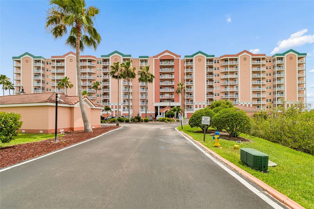 A multi-story peach-colored apartment building stands behind a paved driveway with palm trees — 4516 SEAGULL DRIVE UNIT 416, NEW PORT RICHEY, FL