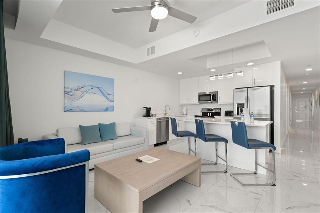 A modern open-concept living room and kitchen featuring white cabinetry, stainless appliances, and blue furniture — 11500 GULF BOULEVARD UNIT 304, TREASURE ISLAND, FL